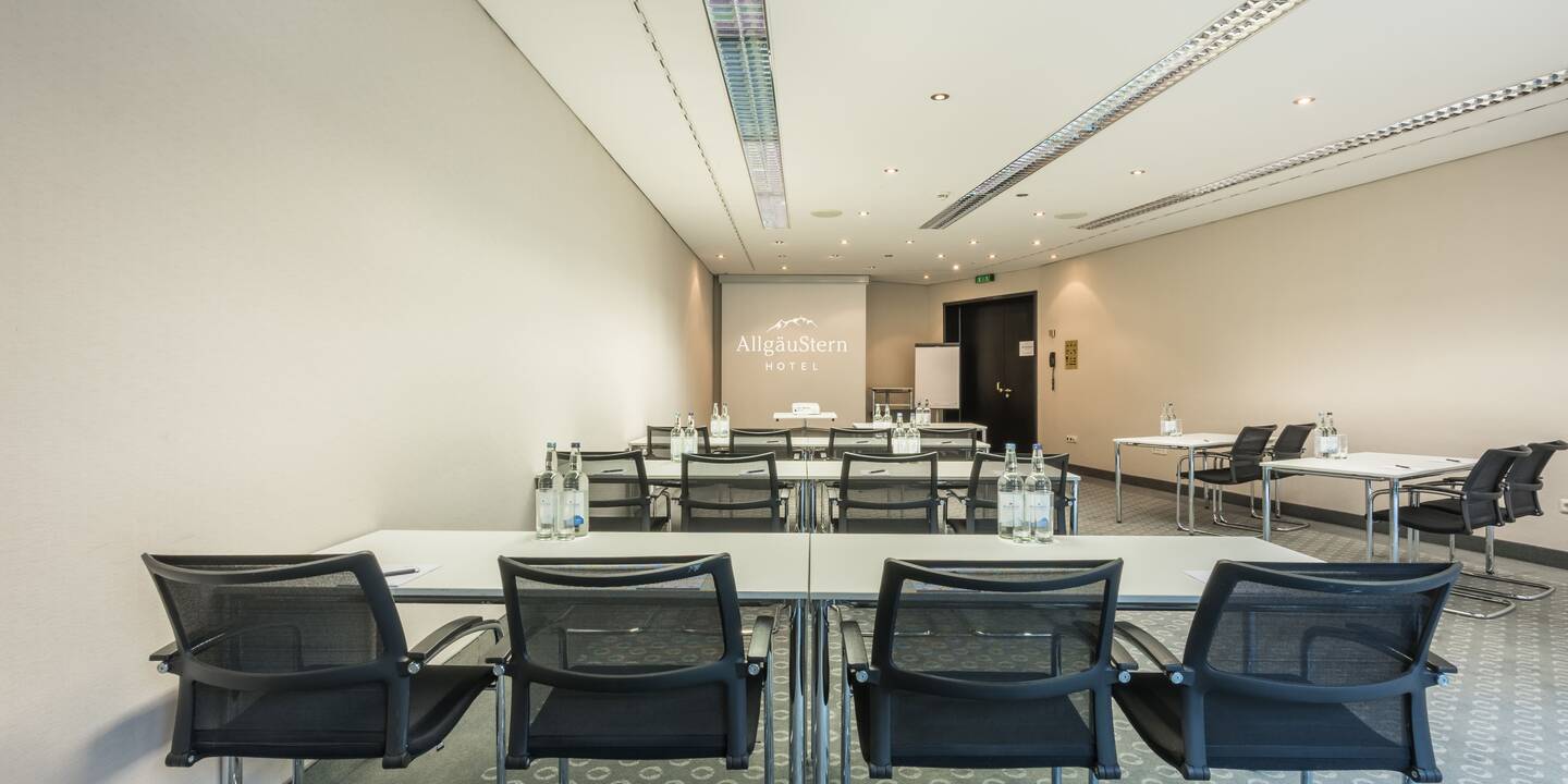 Tagungssalon im AlpenCongressCenter des AllgäuSternHotels Tischreihen und Leinwand am Raumeingang.