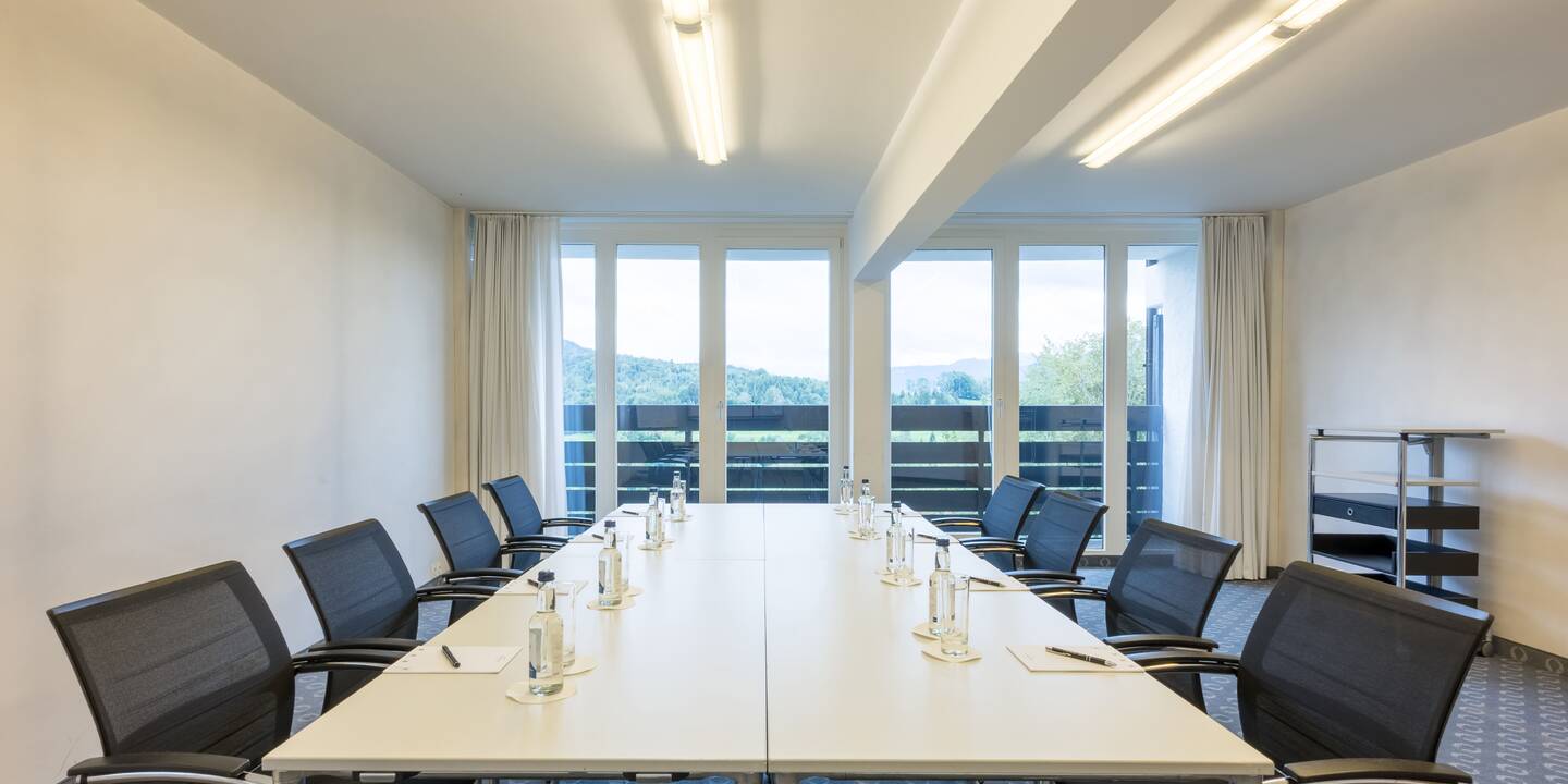 Blick über einen eingedeckten Tischblock in Richtung Balkon mit Naturblick.