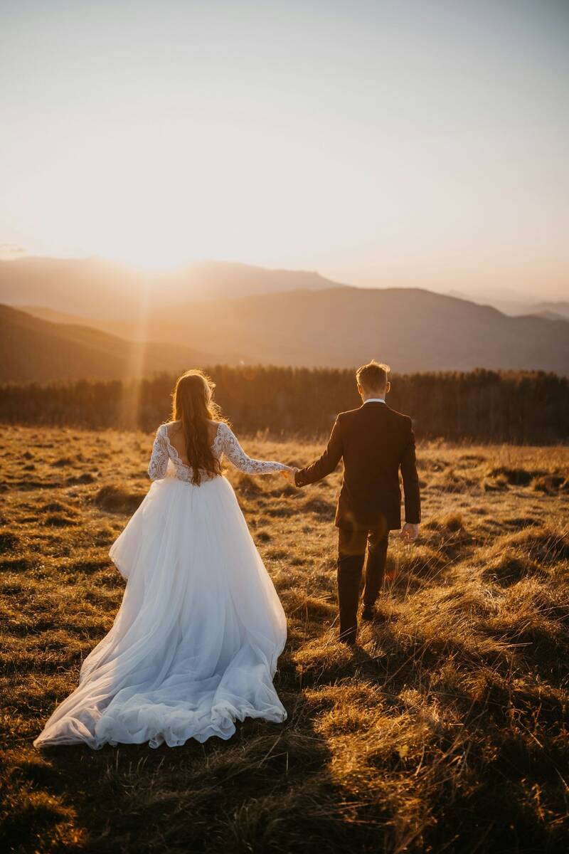 Ein Brautpaar läuft auf einer Bergwiese dem Sonnenuntergang entgegen.