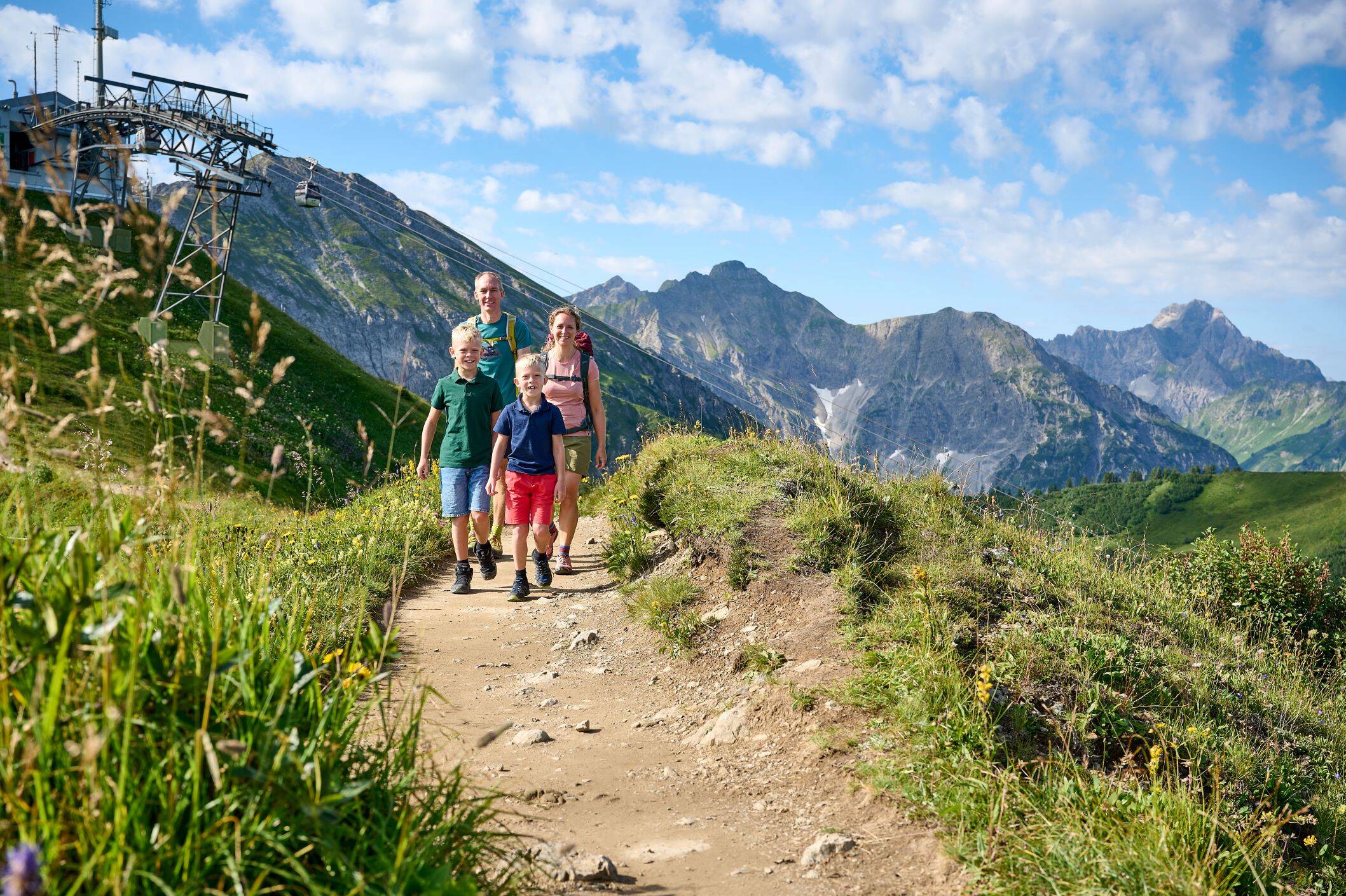 Eine Familie mit zwei Kindern wandert im Sommer auf einem Bergweg.