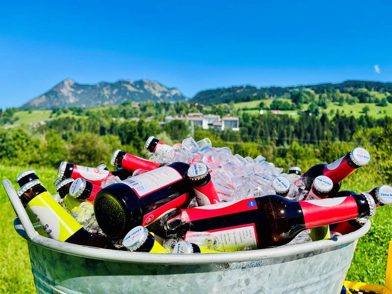 Eine mit Eis und Allgäuer Bier gefüllte Wanne steht auf einer grünen Wiese mit Blick auf das AllgäuSternHotel.