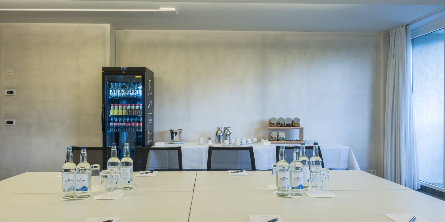 Blick über eingedeckte Tagungstische in Richtung Getränke-Kühlschrank und vorbereiteter Kaffeepause.