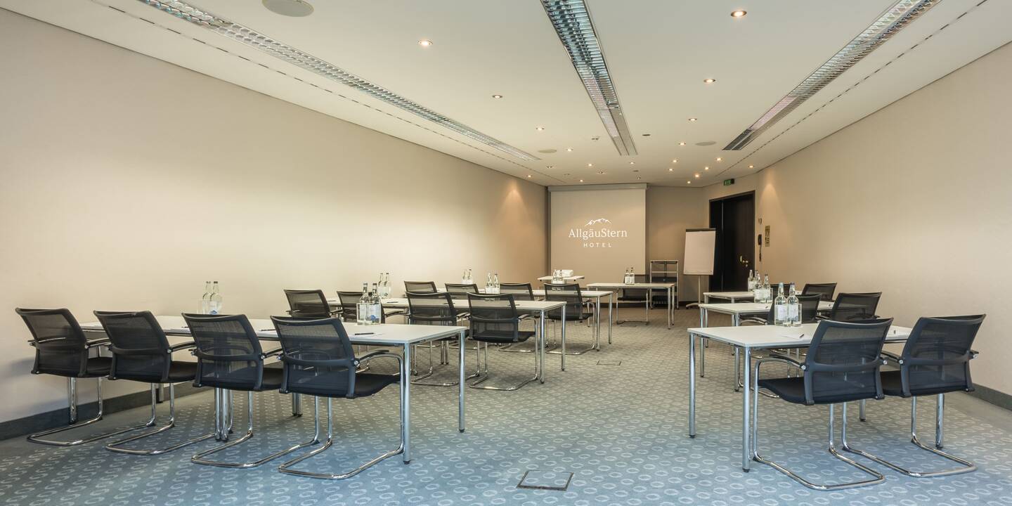 Tagungssalon im AllgäuSternHotel mit Tischreihen und Leinwand.