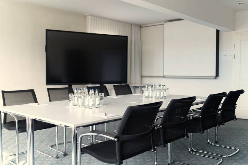 Im Tagungsraum im AllgäuSternHotel stehen mehrere Stühle, ein Konferenztisch und ein großer Monitor für Präsentationen.