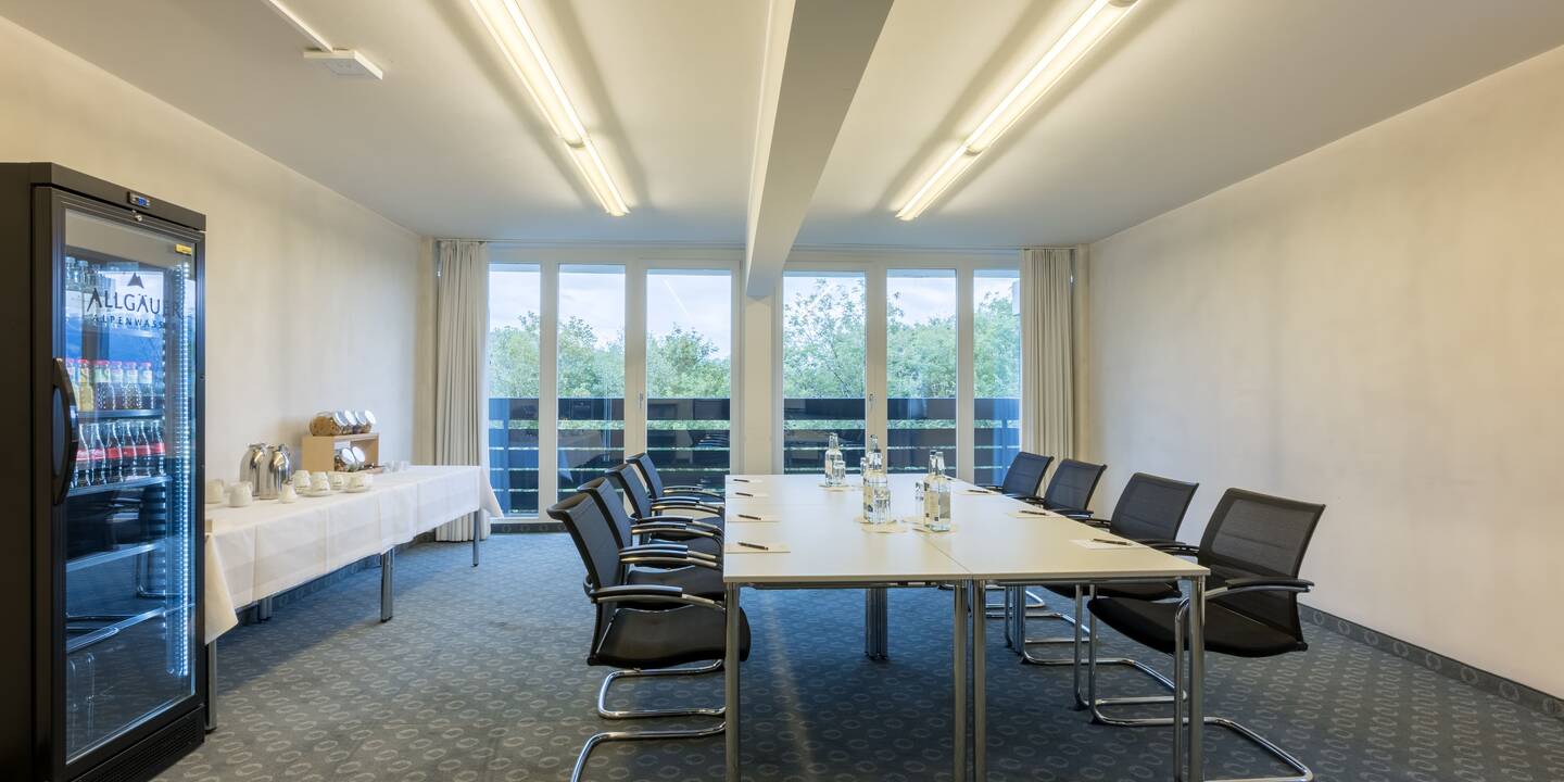 Workshopraum im AllgäuSternHotel mit angerichteter Candybar, gefülltem Kühlschrank und Tischblöcken in der Mitte des Raums, der Blick geht auf den Balkon.